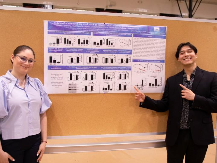 Two students stand in front of thesis project on poster board